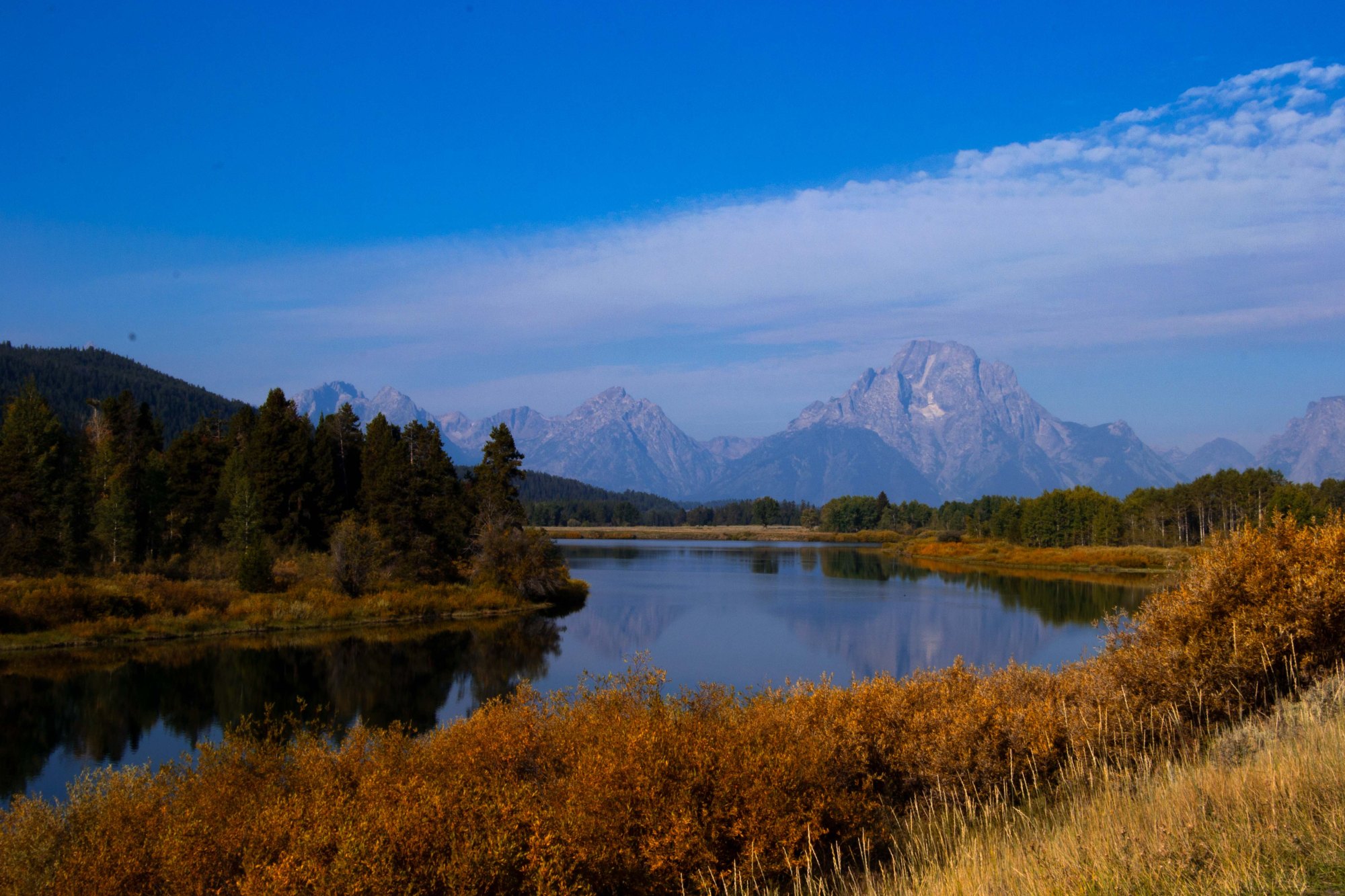 A broad river winds through golden willows with a large square mountain in background.